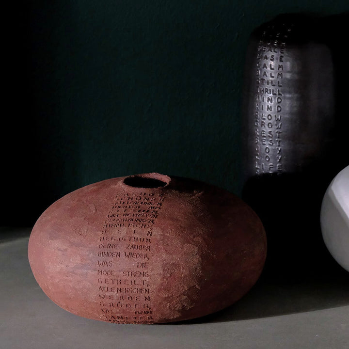 Vase aus Keramik, rund und bauchig aus rotem Steinzeug Ton mit Schillers Ode "And die Freude" als Relief von oben nach unten verlaufend auf der Vase angebracht. Im Hintergrund steht eine weitere Vase von Marie Martin.